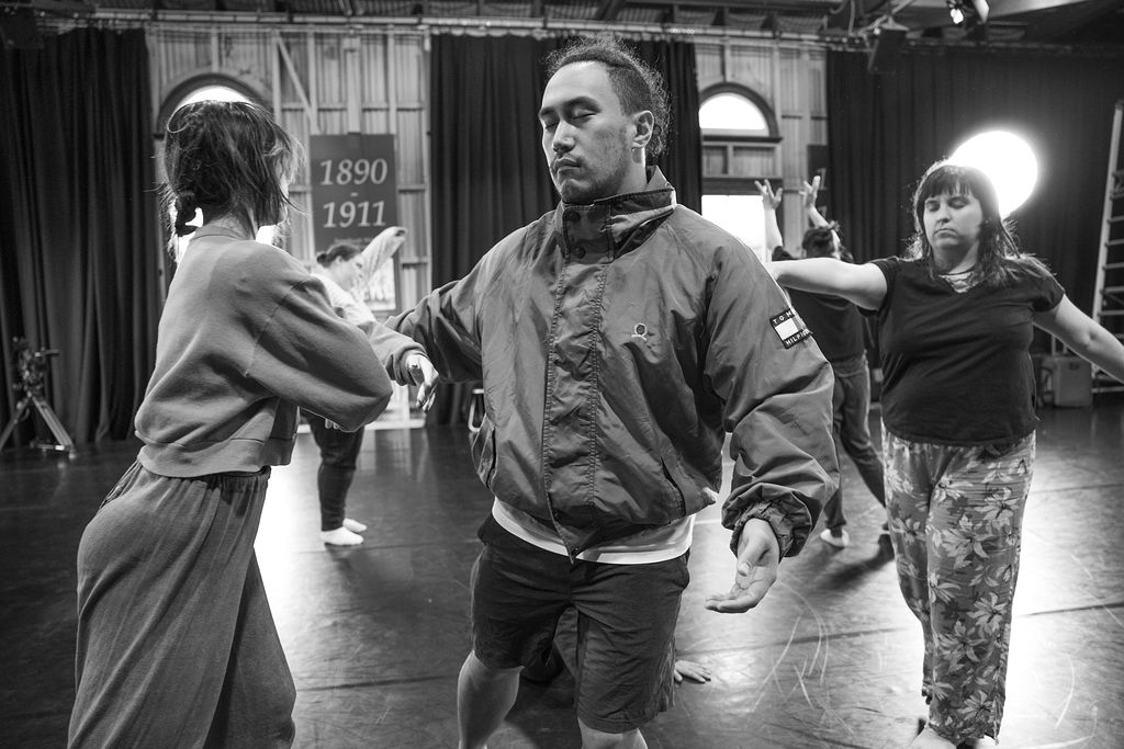 A black-and-white photo of 5 people in a dance studio. They have their eyes closed and are sensing each other's presence. Photo by Natalie Cartney