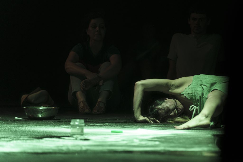 Woman is on the ground with one leg in front of her and one arm above her head, making a perfect angle with the ground. She has her mouth open and hair across her face. Salt is scattered across the ground.