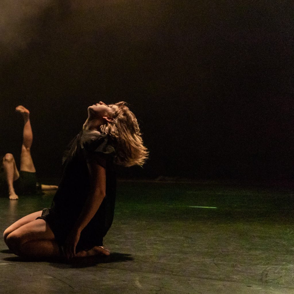 Dancer kneeling on the ground gazing up to the light above.