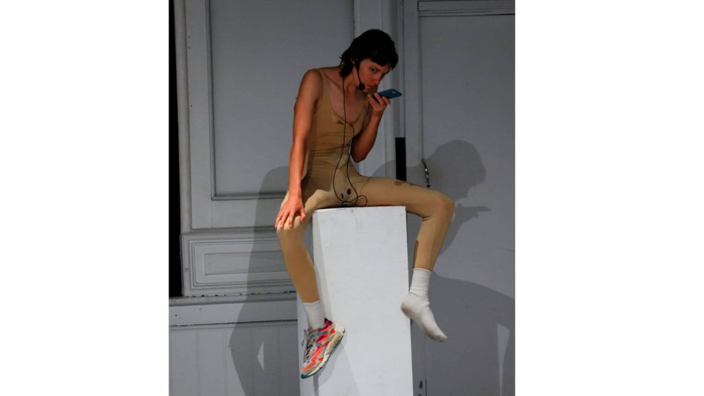 Person sitting on a plinth holding a phone listening intently and wearing only one shoe.