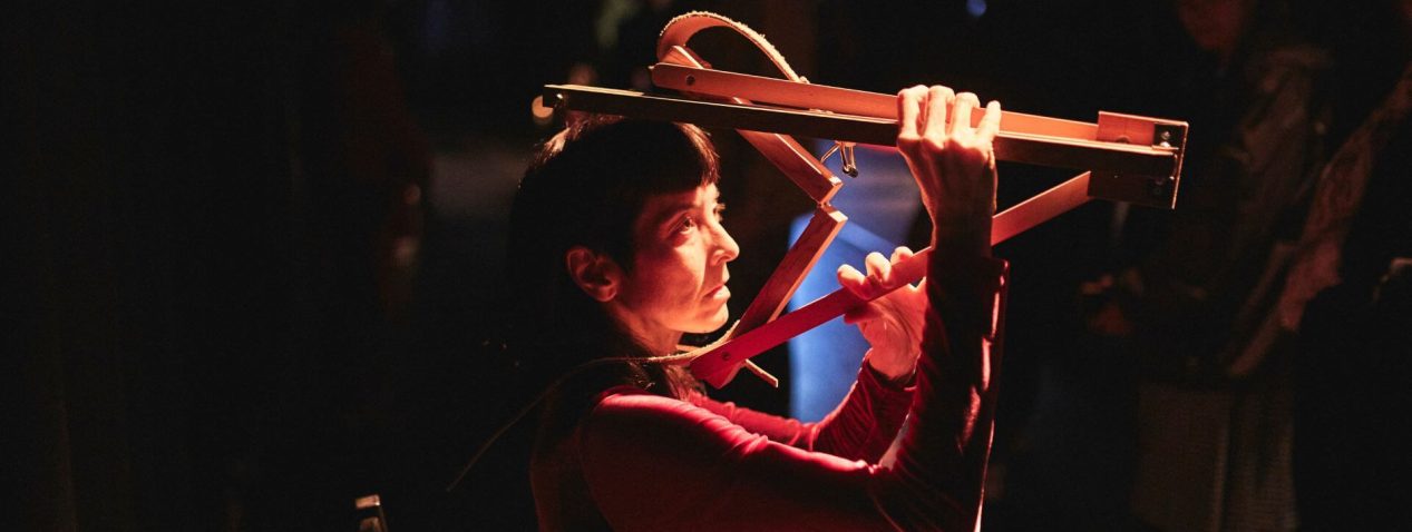 Photograph of a person performing with a wooden object like a painter's easel folded around their head.