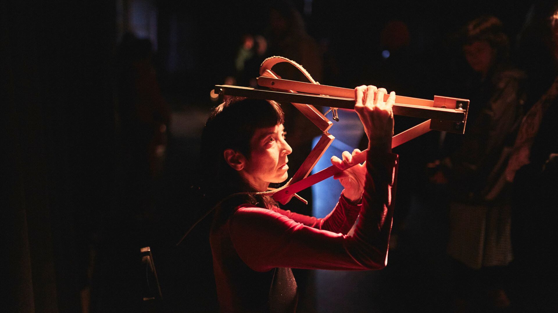 Photograph of a person performing with a wooden object like a painter's easel folded around their head.