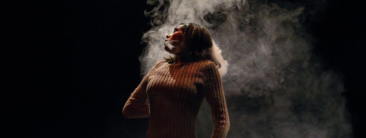 an evocative image of a dancer leaning back slightly and looking to the side with smoke rising behind them.