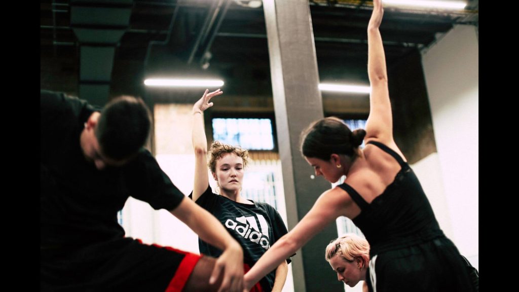 A photo of four dancers close together all facing different directions and with eyes lowered in concentration.