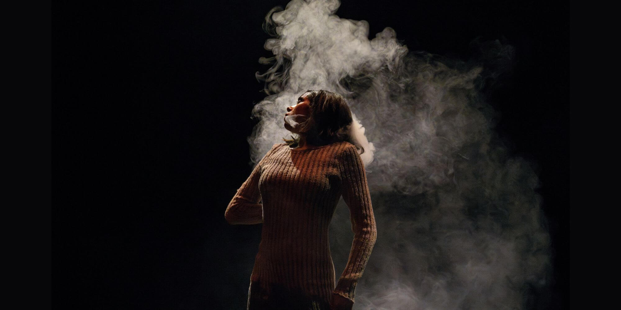 an evocative image of a dancer leaning back slightly and looking to the side with smoke rising behind them.
