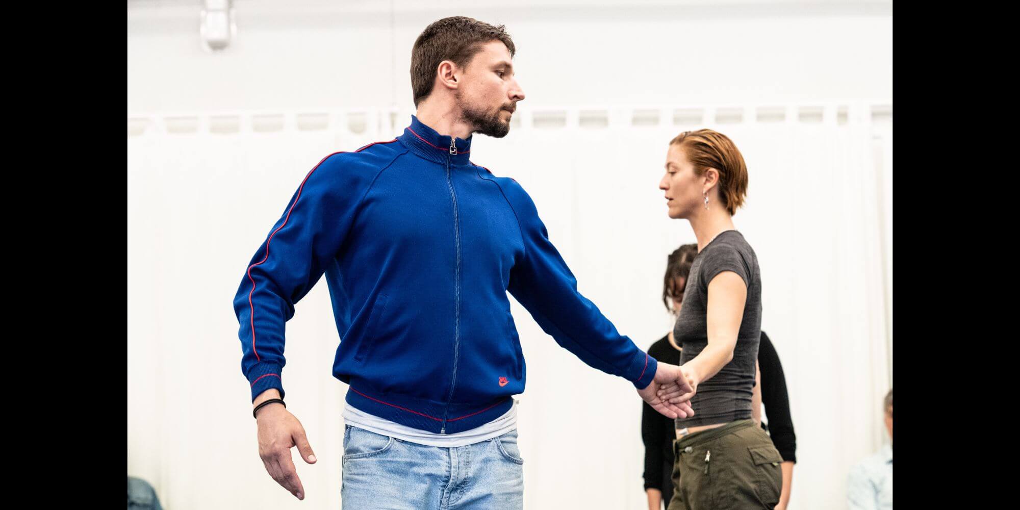 Two dancers move facing different directions and holding hands.
