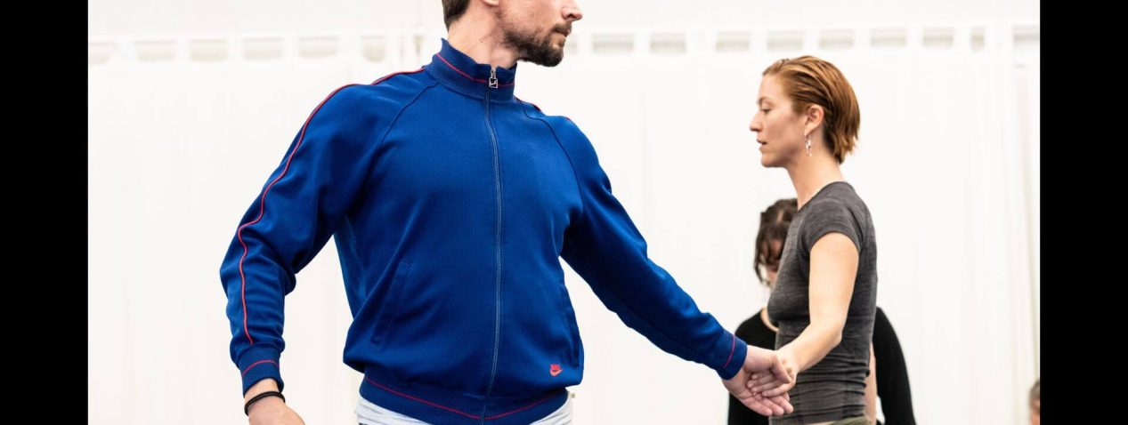 Two dancers move facing different directions and holding hands.