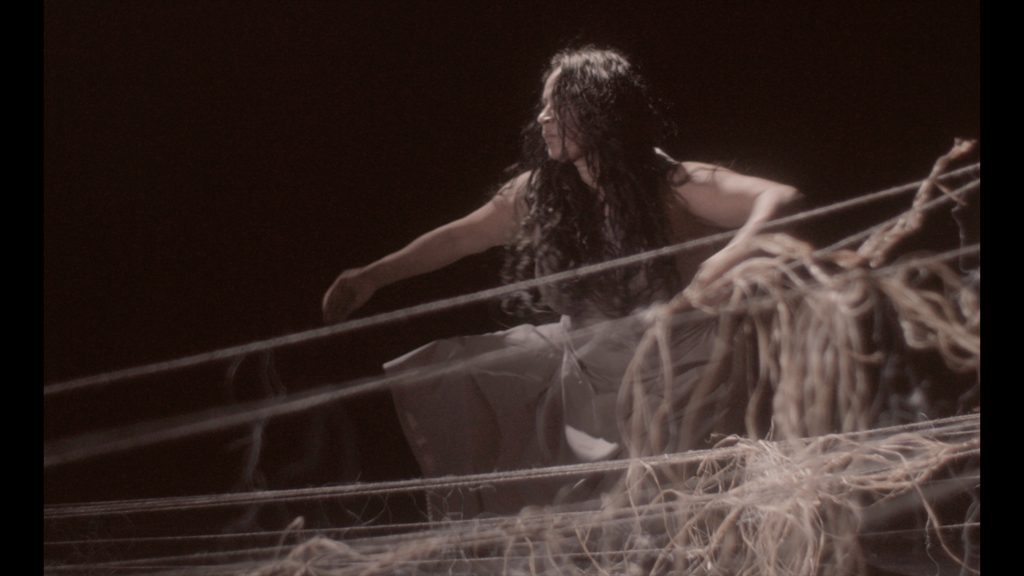 A person dancing; they are bending behind a large delicate structure created from string.