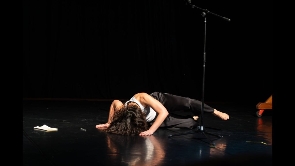 A woman falls to the ground in behind a microphone stand, a notebook and pen also on the ground.