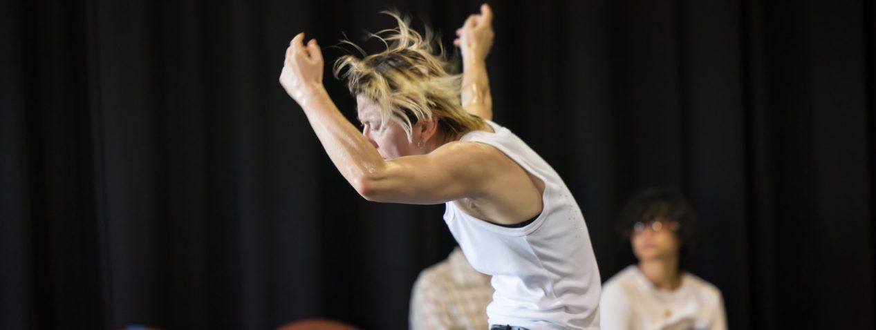 Image of a person dancing with arms above their head, torso rounded, hair flying.