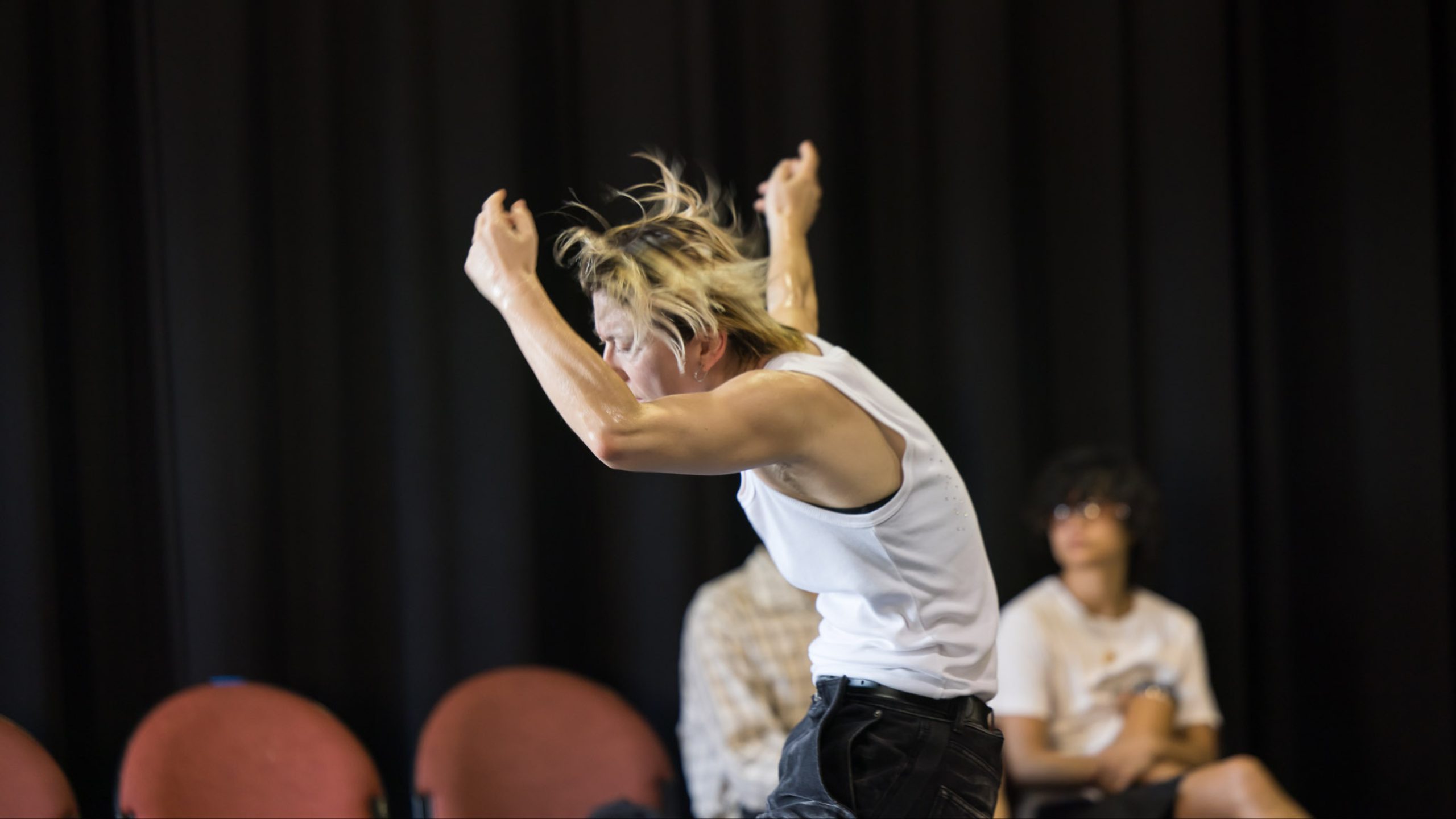 Image of a person dancing with arms above their head, torso rounded, hair flying.