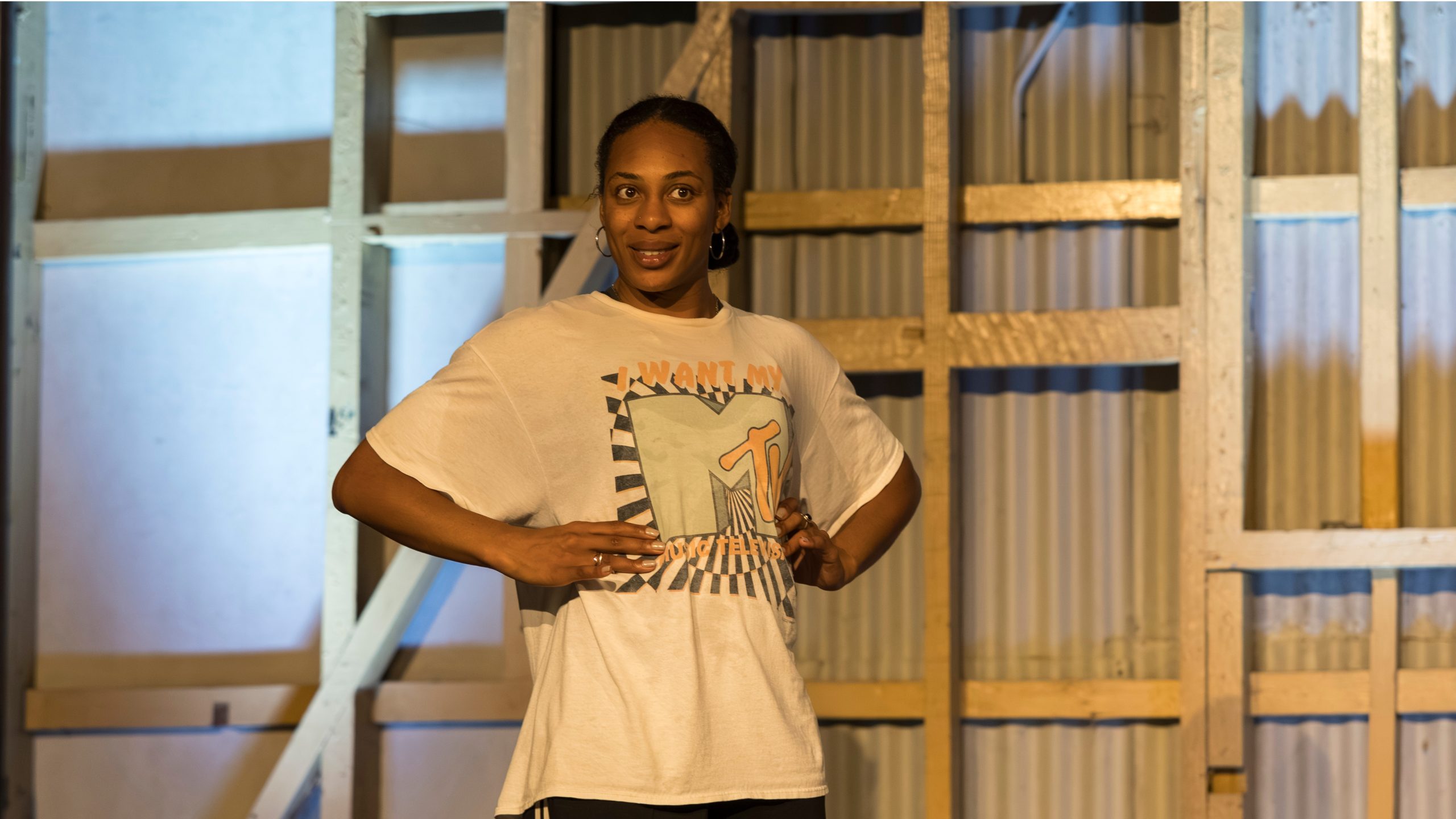 Photograph of a person performing. They have their hands on their waster and are smiling.