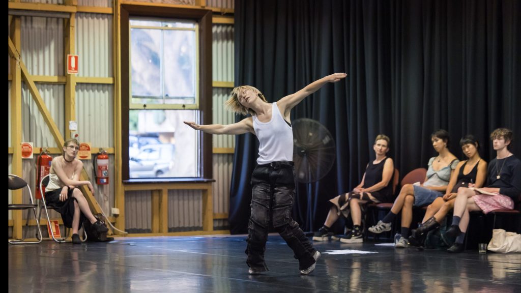 A performer dancing with head tilted to one side, arms outstretched and slightly bent like wings.
