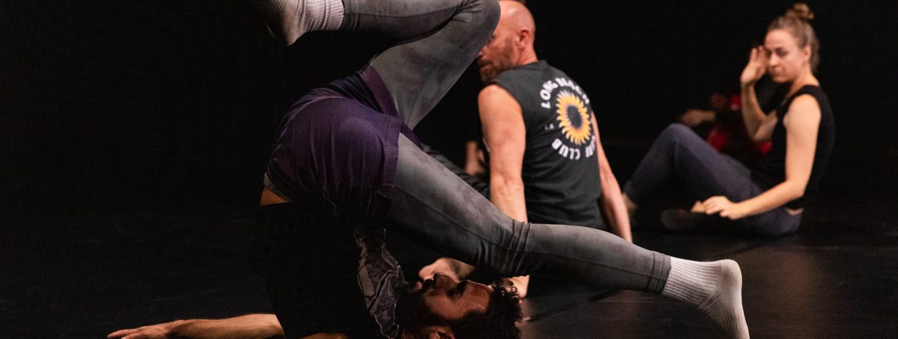 Image of a person dancing. They are balancing on their back and neck with legs in the air and arms pressing into the floor.