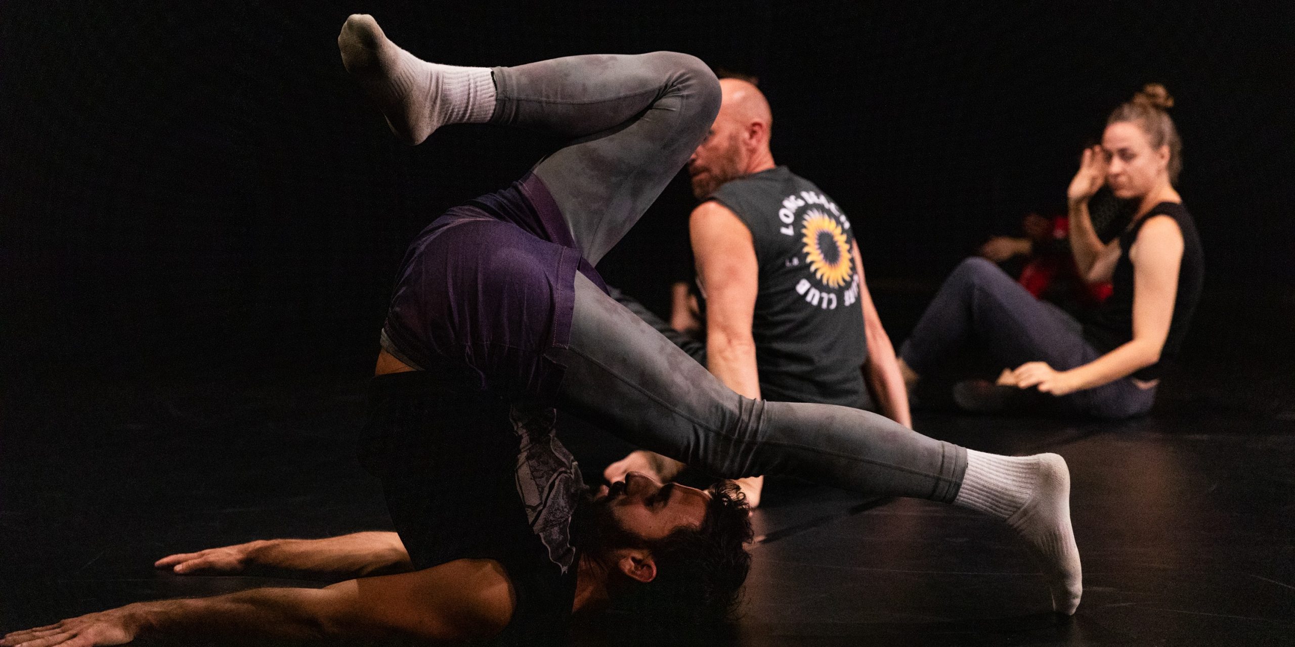 Image of a person dancing. They are balancing on their back and neck with legs in the air and arms presing into the floor.