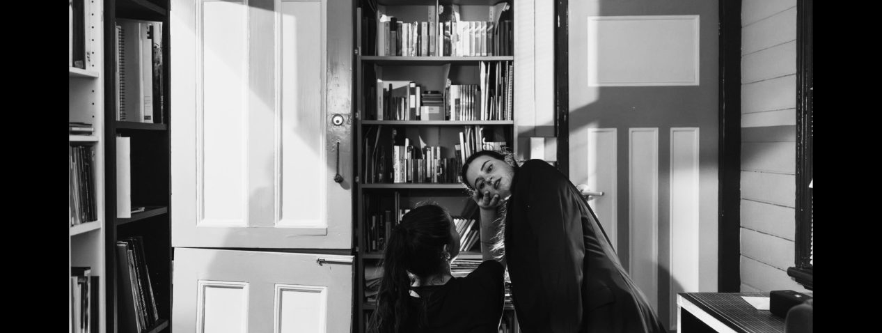 Photo of two people dancing in a small room with bookshelves and a door open.
