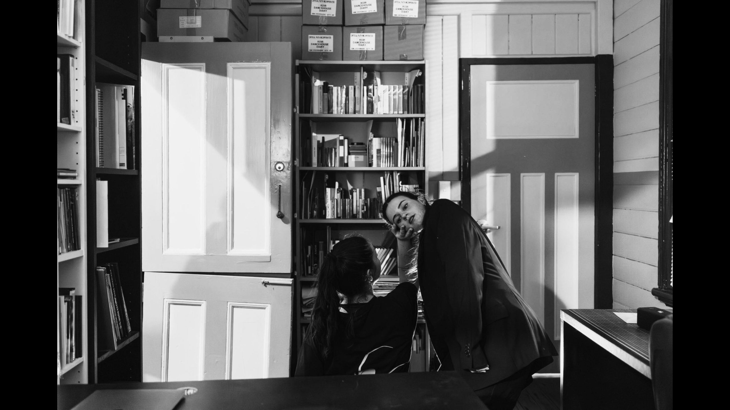 Photo of two people dancing in a small room with bookshelves and a door open.