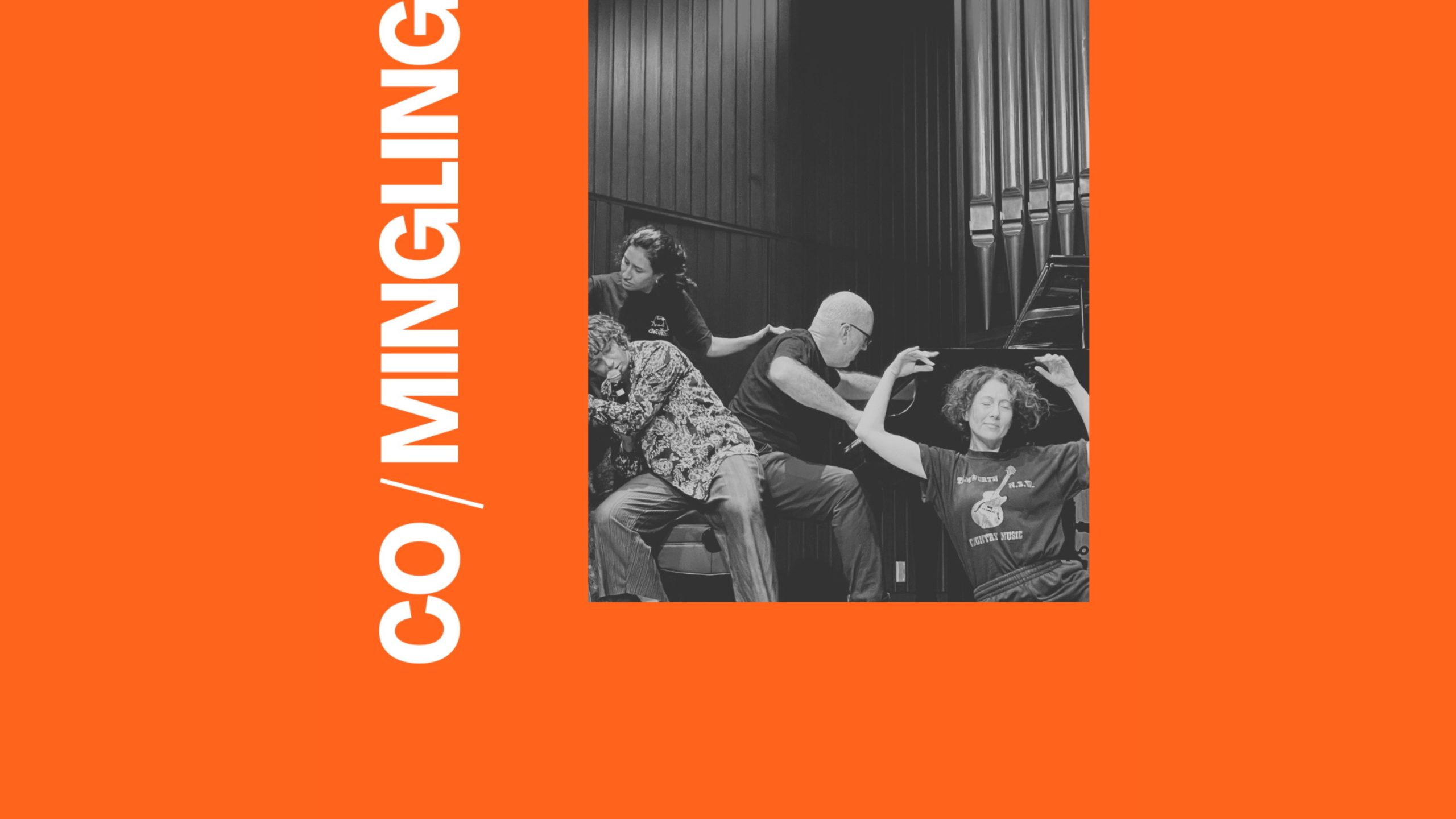 A photo of 5 performers, they are all in physical contact with with at least 2 other performers. One is holding up a microphone up to their lips and another is playing a piano. There are 2 signs saying "Caution, Wet Floor".